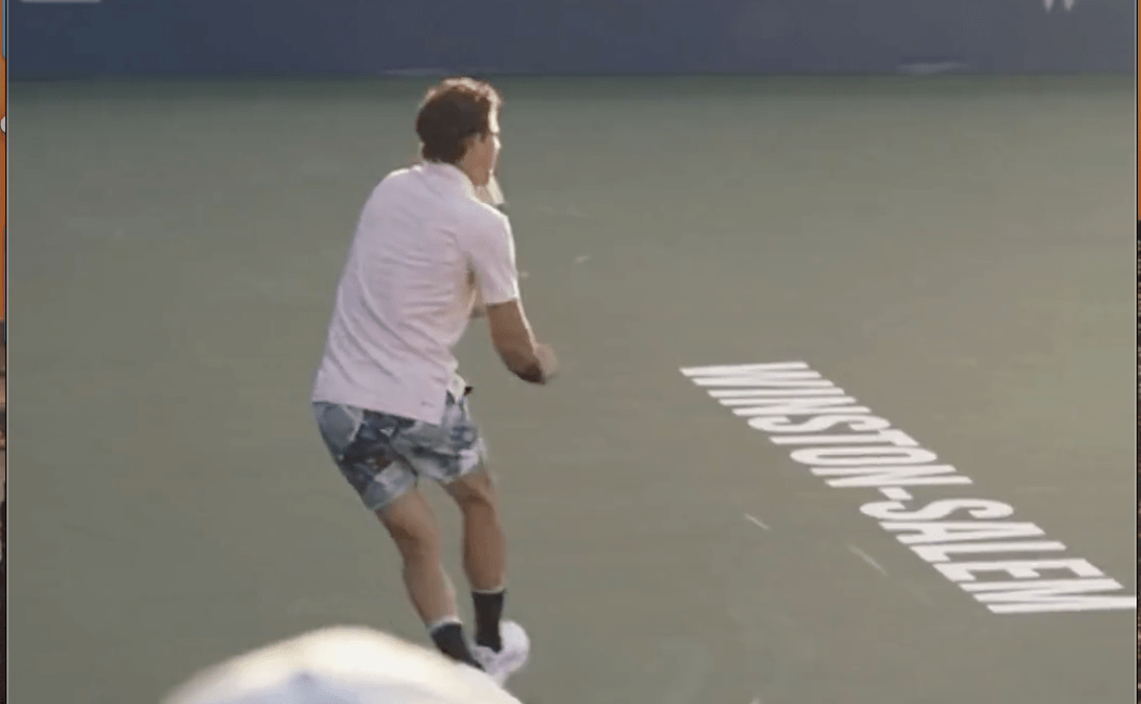 a man in a pink shirt on a green tennis court hitting a ball